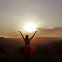 Woman with arms raised standing against sky during sunny day