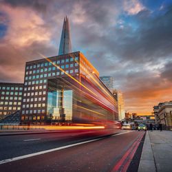 Light trails on road by the shard against cloudy sky at sunset