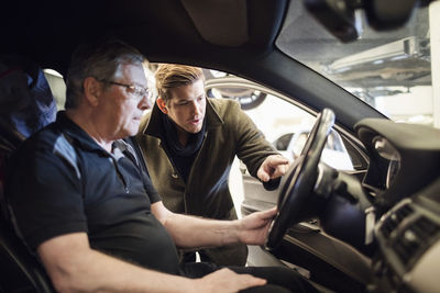 Male customer discussing with mechanic sitting in car at repair shop