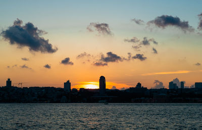 Sea by buildings against sky during sunset