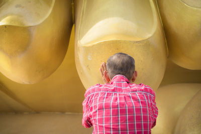 Rear view of man touching golden buddha statue