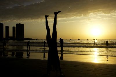 Silhouette people on beach against sky during sunset