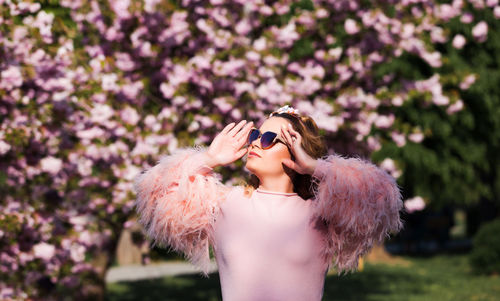Woman wearing sunglasses standing against pink flowers