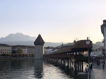 Bridge over river by buildings against sky during sunset