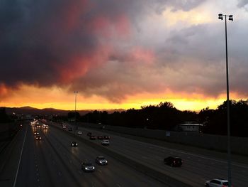 Cars on road against dramatic sky during sunset