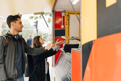 Male and female friends receiving meal from food truck in city