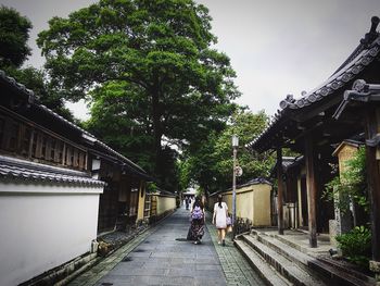 People walking on road amidst trees against sky