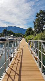 Footbridge leading towards mountains against sky