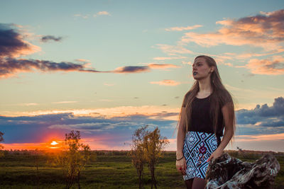 Young woman standing on field against sky during sunset