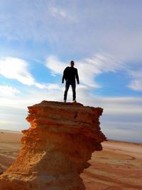 Low angle view of man standing on rock against cloudy sky