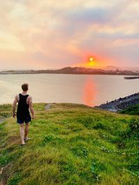 Man walking at beach against sky during sunset