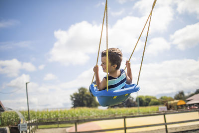 Low angle view of boy swinging outdoors on blue swing at playground. on the move
