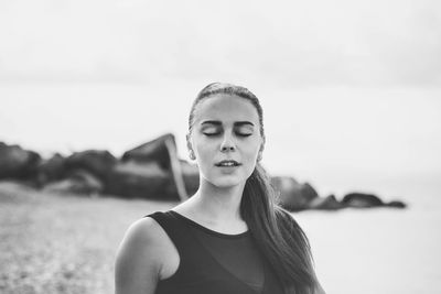 Close-up of young woman with eyes closed standing at beach against sky