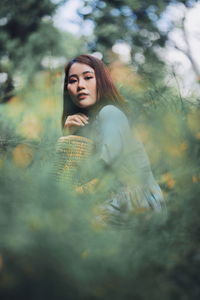 Side view portrait of young woman crouching amidst plants on field