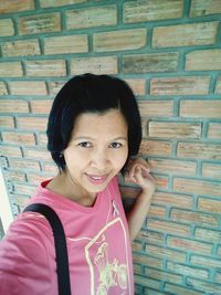 Portrait of smiling girl standing against brick wall