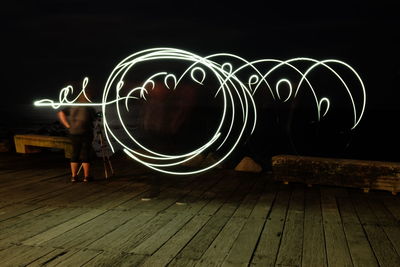 Rear view of woman standing by illuminated light against sky at night