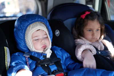 Siblings sitting in safety chairs in the back seat of a car