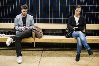 Full length of people using technologies on bench at subway station