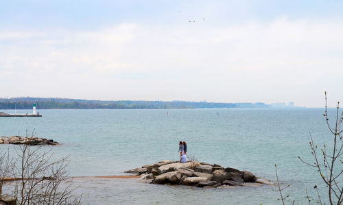 Female friends sitting on rocks in sea against sky