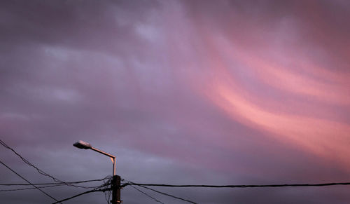 Low angle view of silhouette electricity pylon against dramatic sky