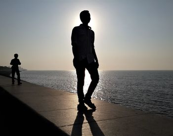 Silhouette man walking on beach against clear sky