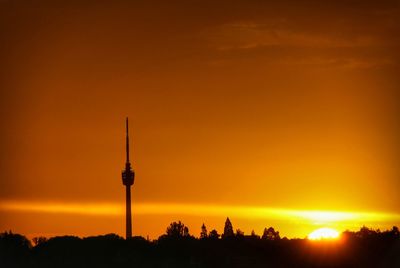 Silhouette of communications tower in city during sunset