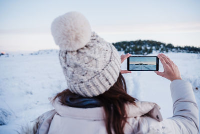 Rear view of person photographing with mobile phone in winter