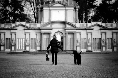 Full length rear view of woman walking with dog against building