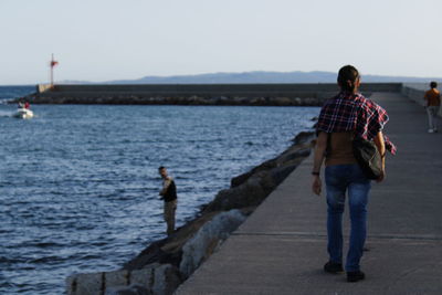 Rear view of man walking on sea against clear sky