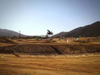 Person practicing stunt on motorcycle over landscape against clear sky