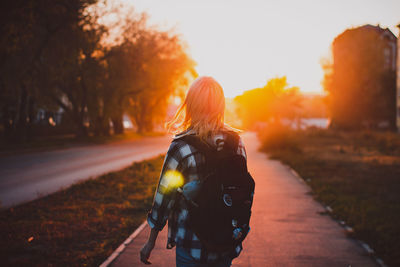 Rear view of woman standing on road against sky during sunset