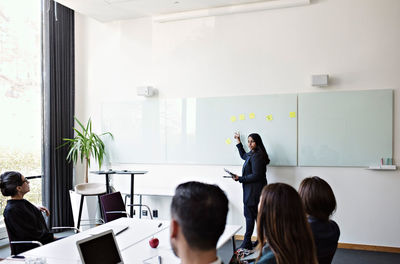 Businesswoman gesturing over whiteboard while discussing with colleagues during meeting in office