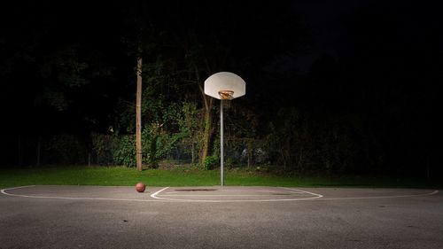 Street light and basketball hoop on field by trees at night