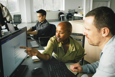 Businesswoman pointing at computer while discussing with male colleague at office