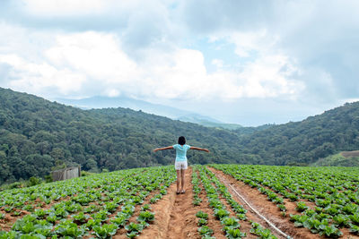 Full length of woman with arms outstretched standing on agricultural field against sky