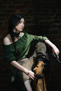 Thoughtful young woman with gun sitting against wall
