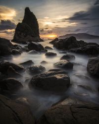 Rocks in sea against sky during sunset