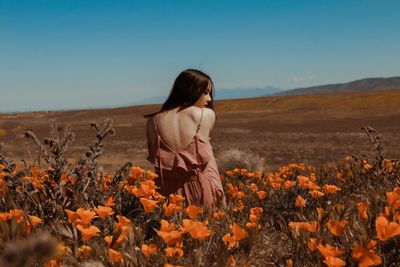 Rear view of woman sitting on field against clear sky