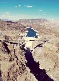 Hoover dam bridge amidst rocky mountains against sky on sunny day