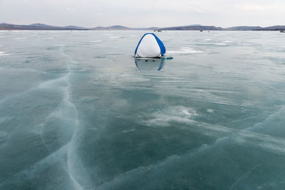 A fisherman's tent stands on the ice of a melting lake, covered with cracks, in early spring.