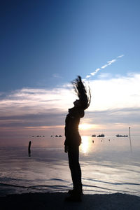 Silhouette woman standing on beach against sky during sunset