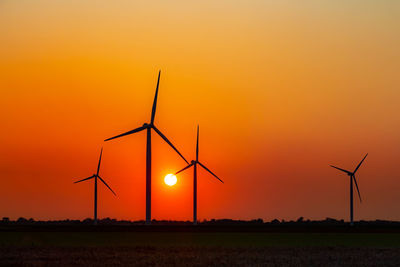 Silhouette wind turbines on field against orange sky