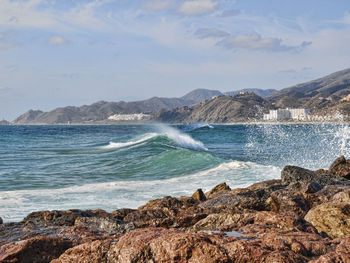 Sea waves splashing on rocks against sky