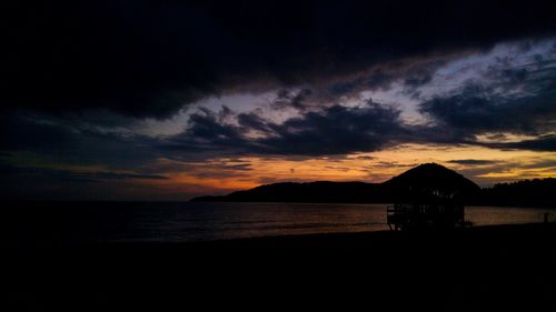 Silhouette beach against dramatic sky during sunset