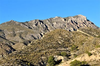 Low angle view of rocky mountains against clear blue sky