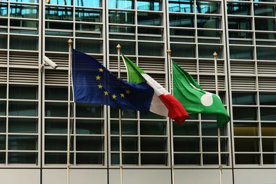 Multi colored flags in the wind hanging on pole against building