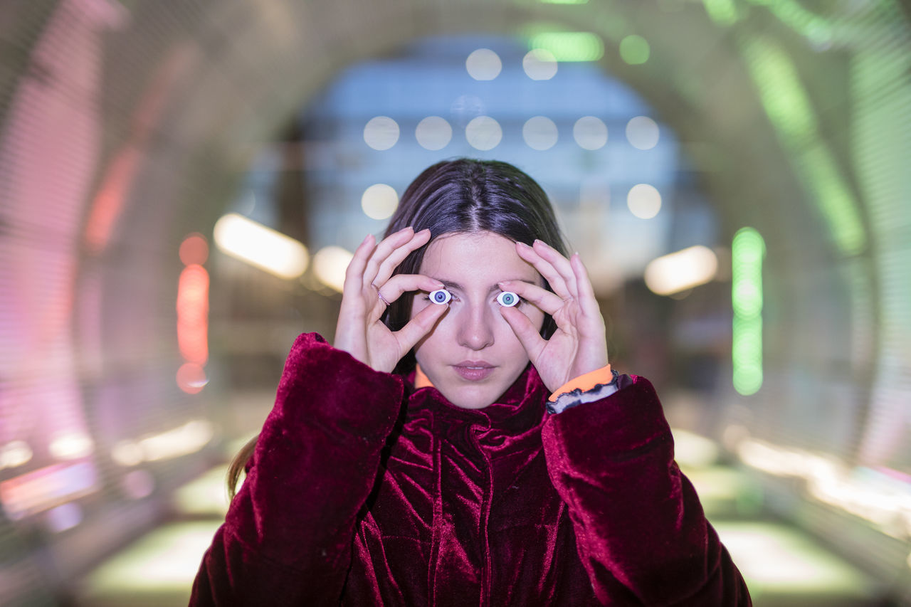 PORTRAIT OF YOUNG WOMAN STANDING IN ILLUMINATED PARK