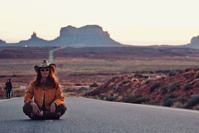 Portrait of man sitting on road against sky