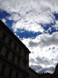 Low angle view of birds flying against cloudy sky