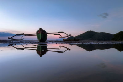 Rear view of man standing by lake against sky during sunset